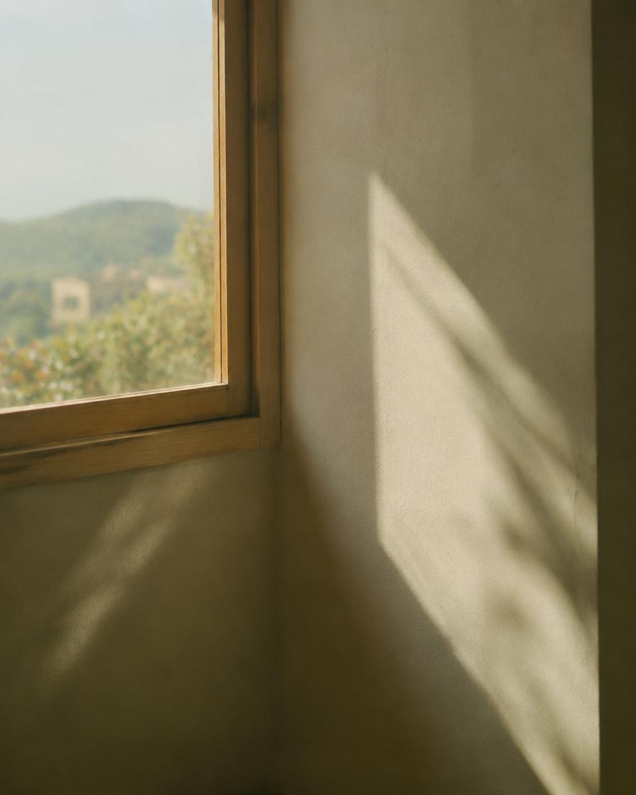 Daylight falling across a plaster wall beside a wooden window